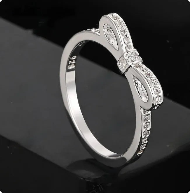Silver coloured bow-shaped ring with sparkling rhinestone and zircon crystal details on a finger.