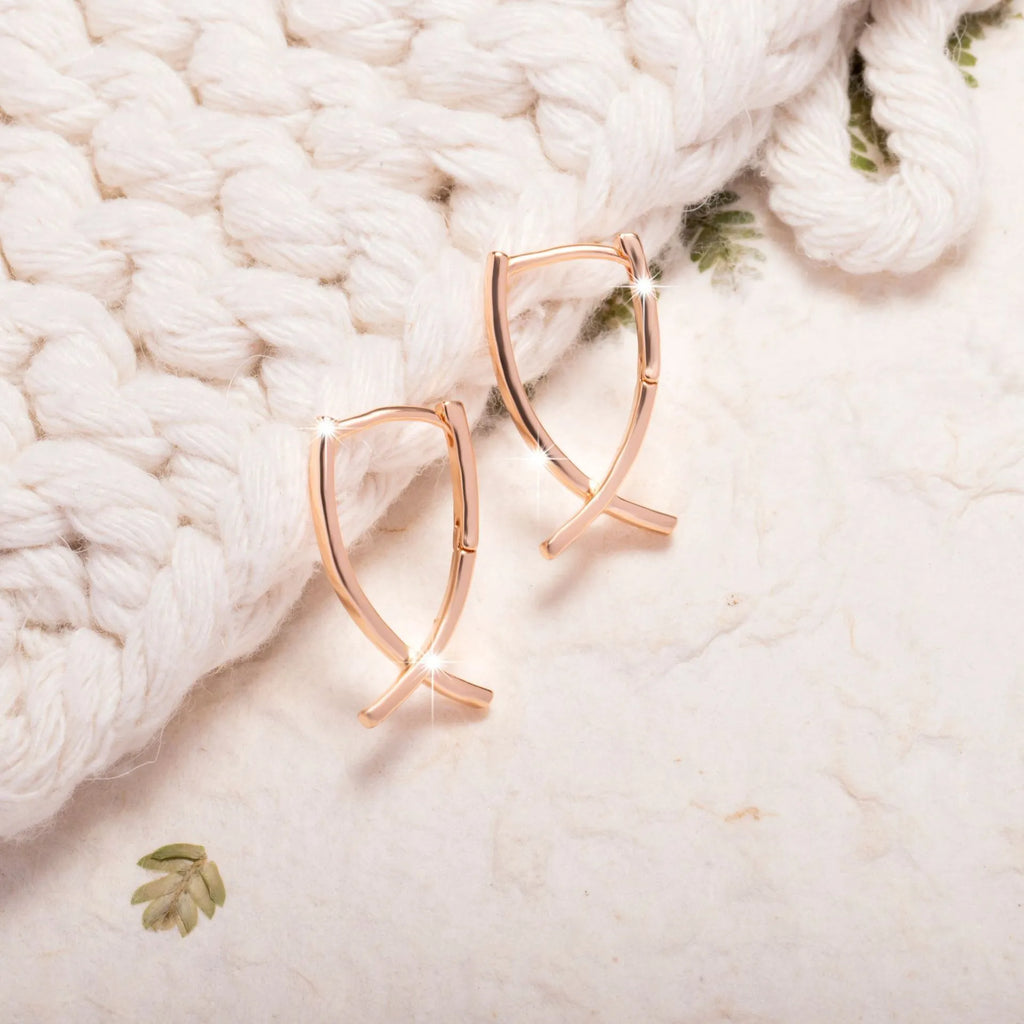 A pair of rose gold cross-shaped earrings made from copper on a white background.