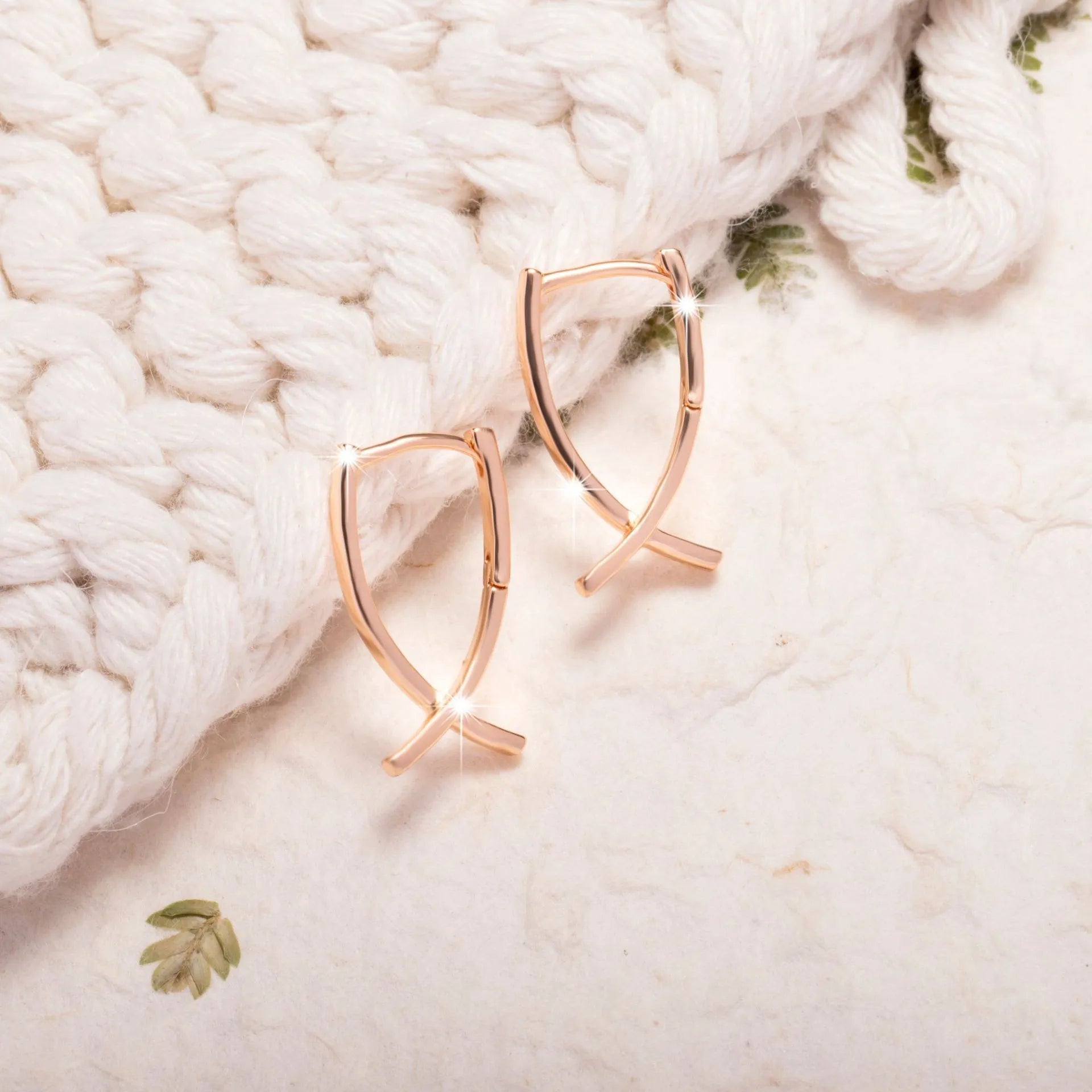 A pair of rose gold cross-shaped earrings made from copper on a white background.