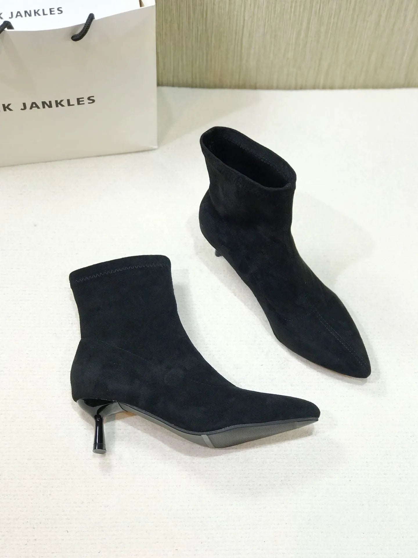 Black pointed toe ankle boots with a high stiletto heel on a woman's foot.