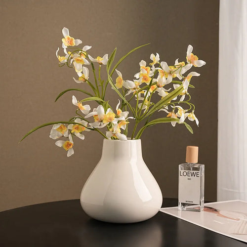 Ceramic round belly vase in black or white with artificial orchid stems on wooden surface