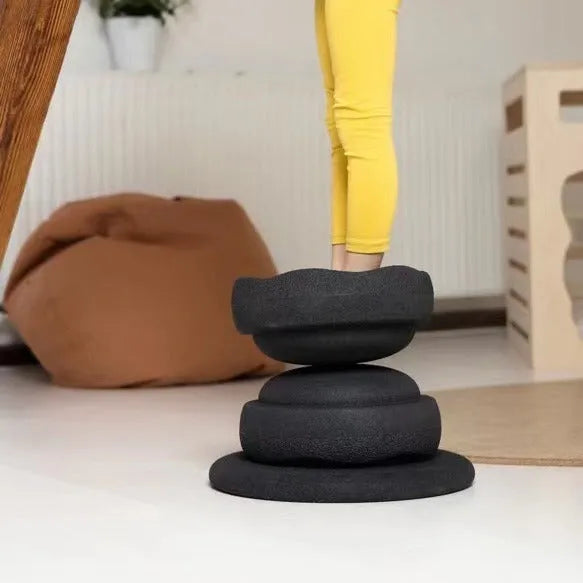 A plastic balance board for children, shown in mixed wood colour and solid black options.