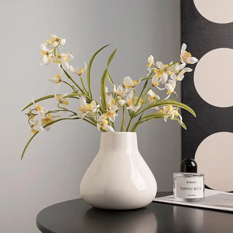 Ceramic round belly vase in black or white with artificial orchid stems on wooden surface