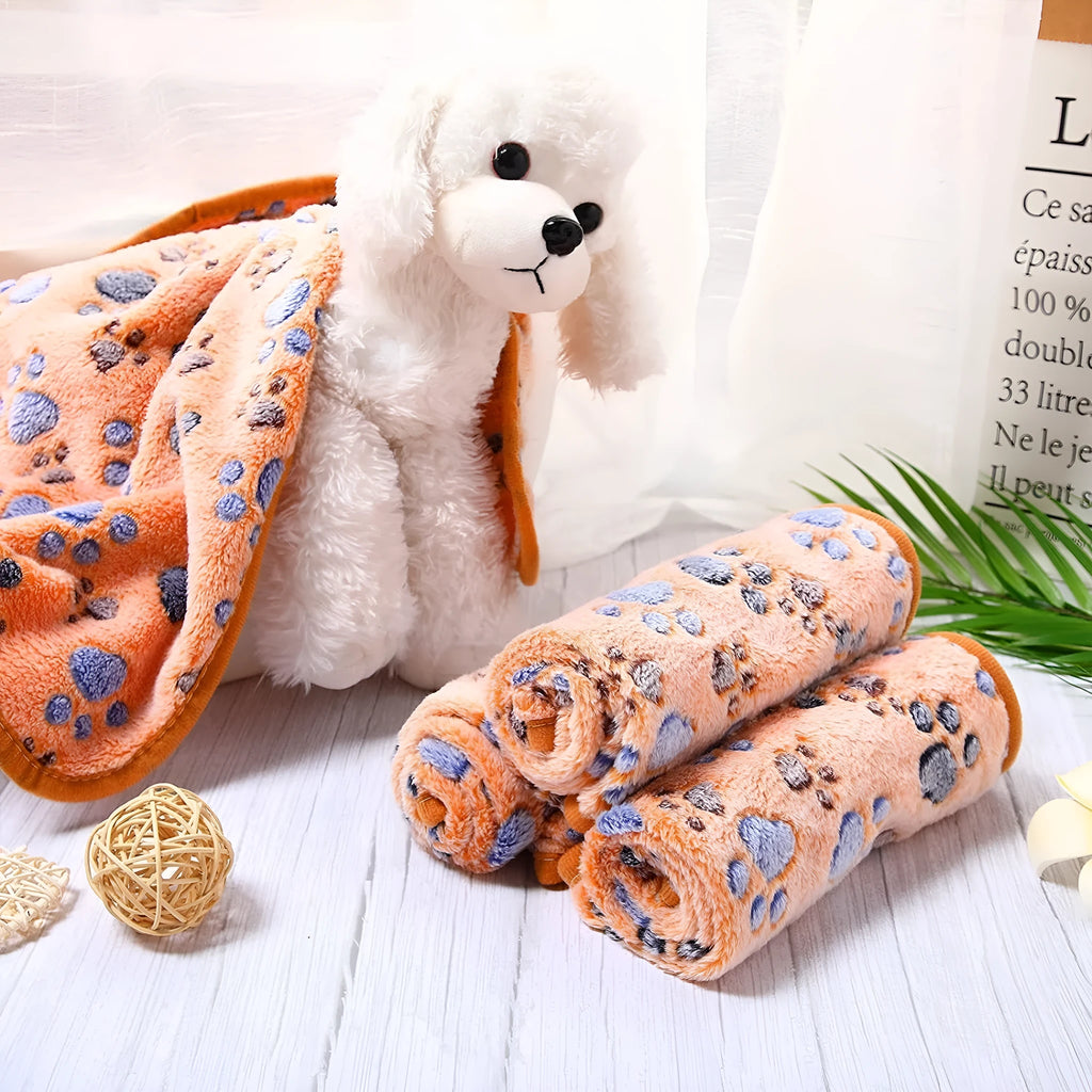 Coral fleece dog blanket with paw print pattern in beige, shown in a large size on a dog bed.