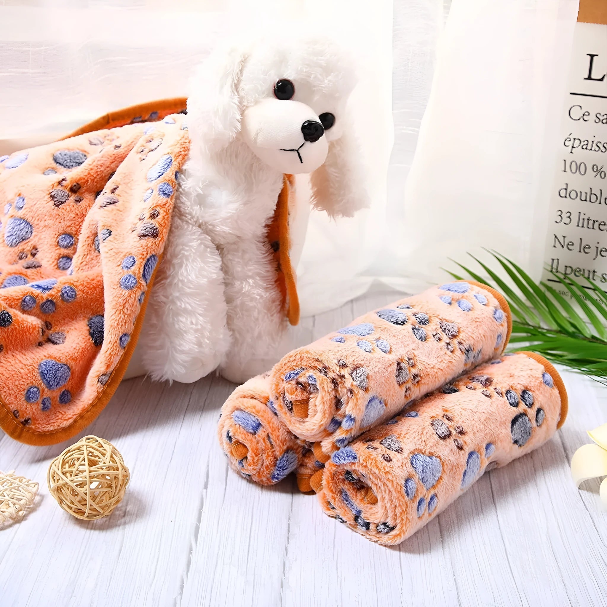 Coral fleece dog blanket with paw print pattern in beige, shown in a large size on a dog bed.