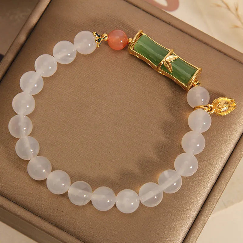 Women's bracelet with white agate bead and bamboo-shaped jade segments on a neutral background.