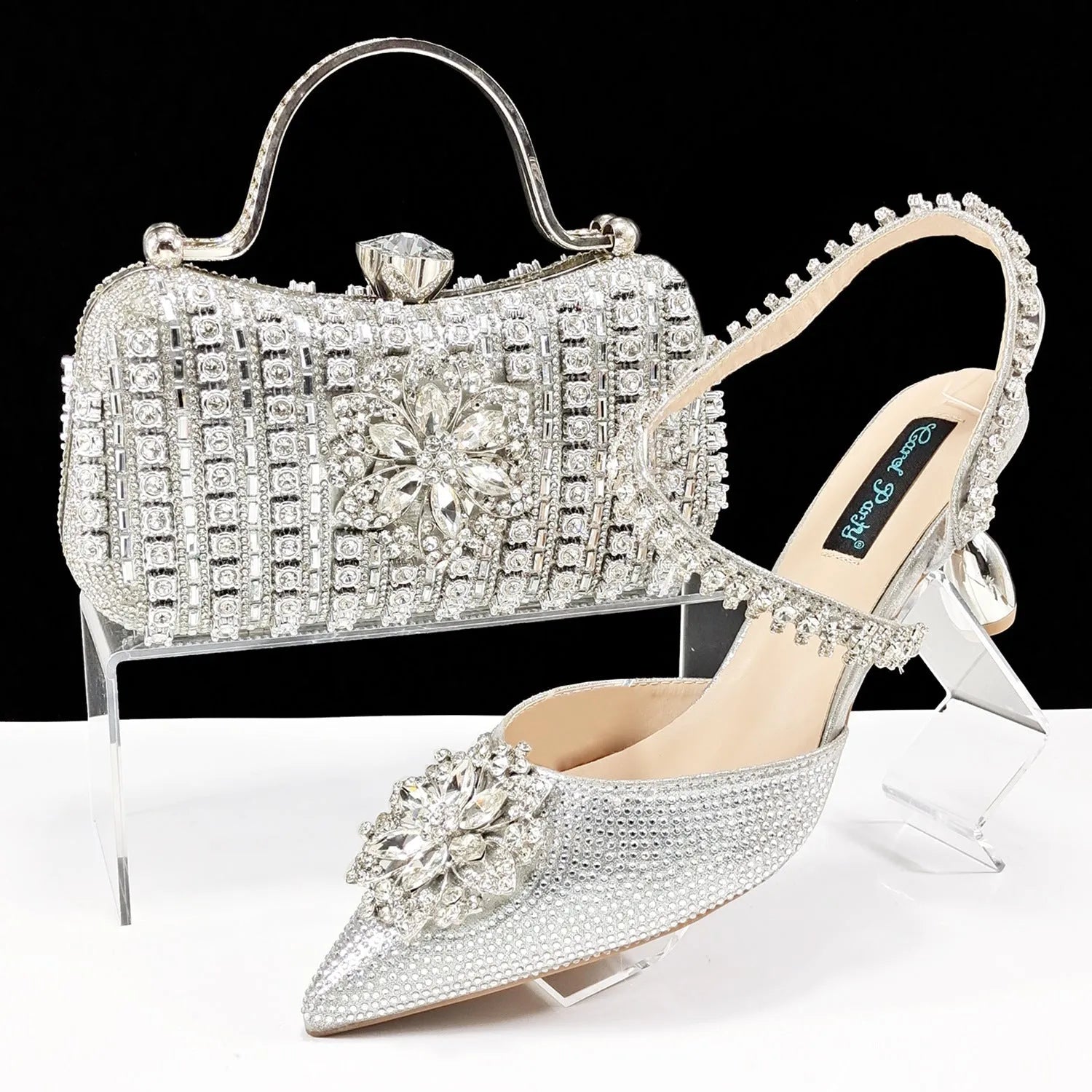 Women's black high heel sandals with ankle chain, floral rhinestone detail, and matching hard clutch bag