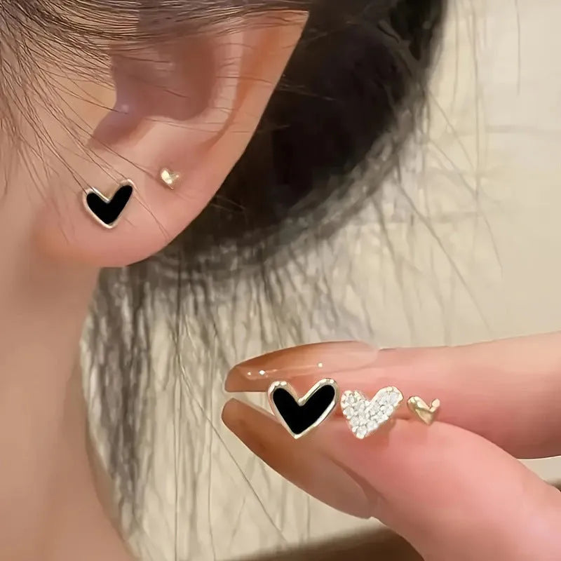 Three pairs of women's heart-shaped alloy earrings in gold, black, black-white, and pink colours