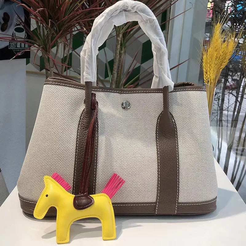 Women's canvas bucket tote bag with leather handles and detailing in black, shown with open top revealing internal zip pocket.