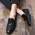 Men's black pointed toe slip on loafers with a tassel detail on the front, shown on a plain background.