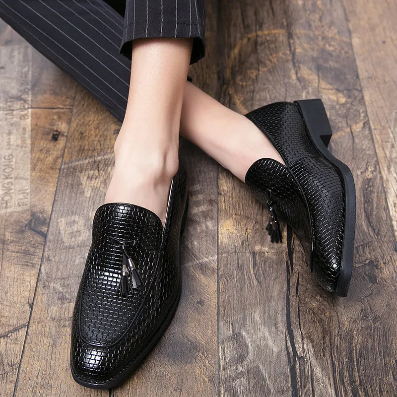 Men's black pointed toe slip on loafers with a tassel detail on the front, shown on a plain background.