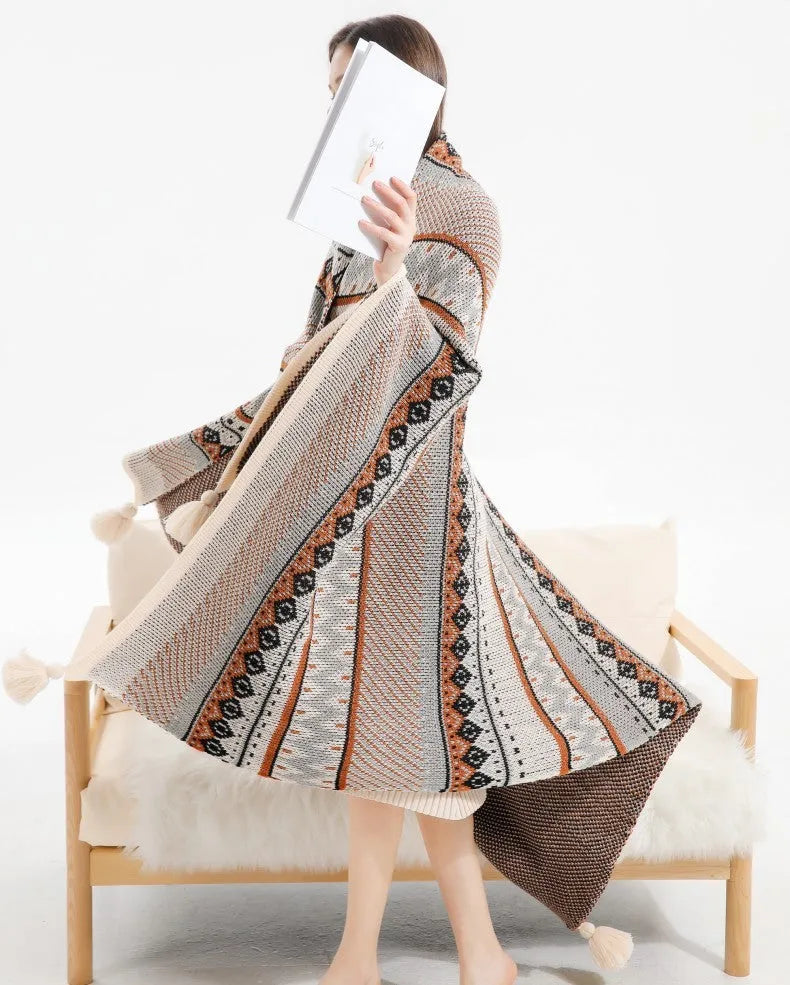 Beige and orange bohemian-style acrylic sofa blanket with tassel fringe on a grey sofa.