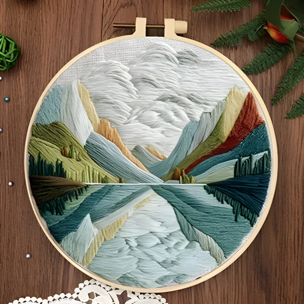 Embroidery kit with printed landscape fabric, thread, bamboo frame, and needles arranged for DIY cloth art