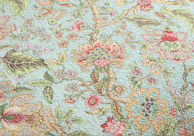 Blue American floral and bird print cotton quilted bedspread set with matching sheet on a bed.