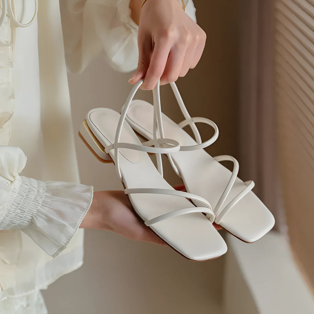 Women's beige flat strap Roman sandals with an open toe and square toe bracket on a white background.