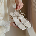 Women's beige flat strap Roman sandals with an open toe and square toe bracket on a white background.