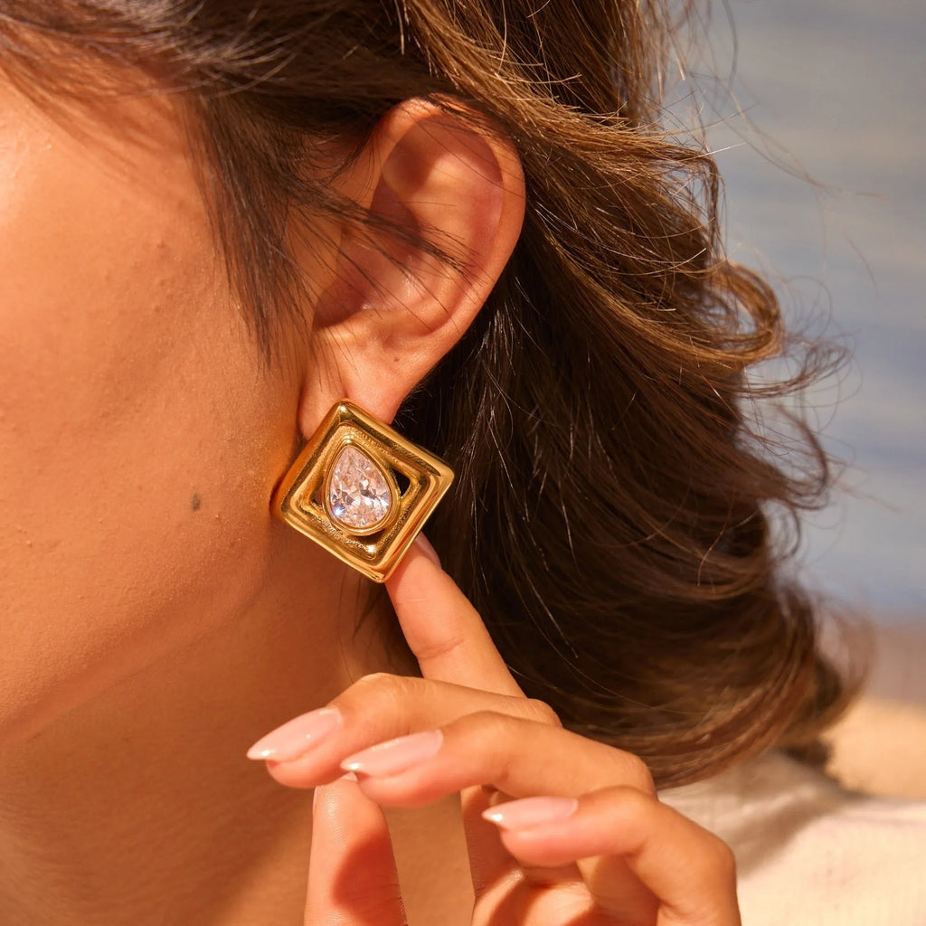 Pair of gold-coloured stainless steel stud earrings with geometric water drop zircon stone inlays.