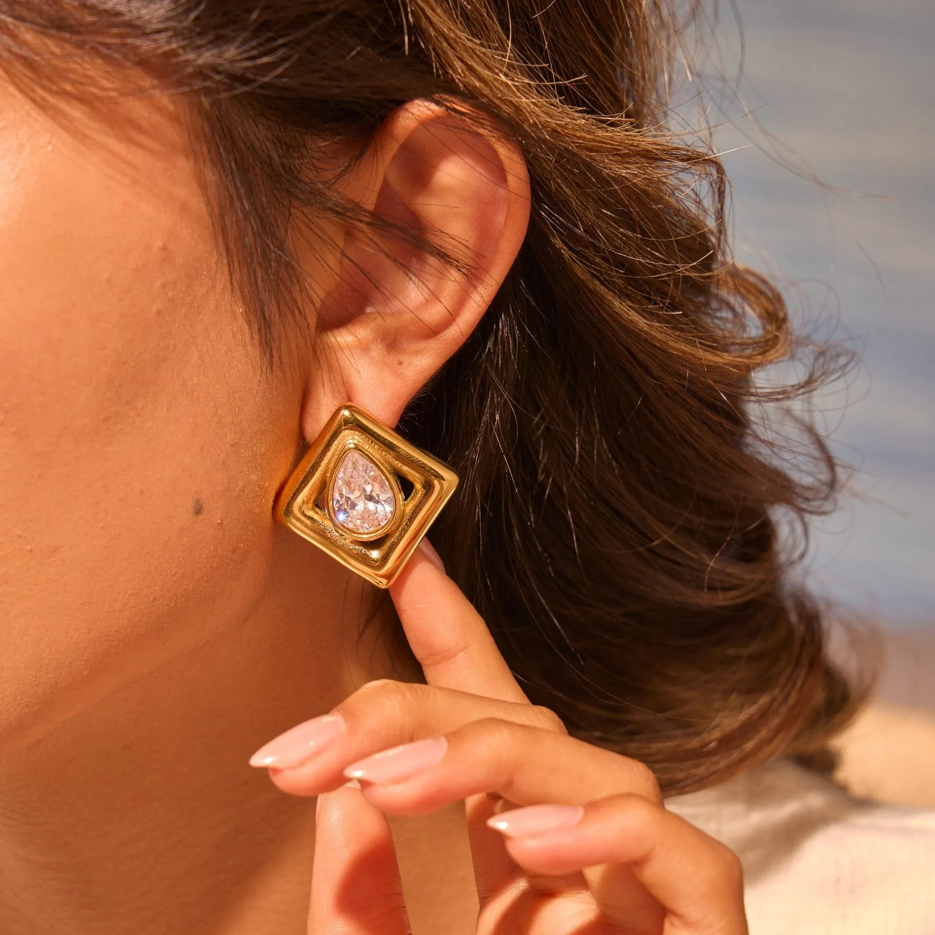 Pair of gold-coloured stainless steel stud earrings with geometric water drop zircon stone inlays.