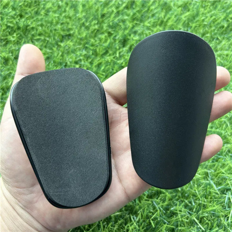 Extra small black and white plastic football shin guards measuring 8x5cm and 10x6cm