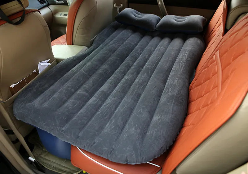 Black inflatable car bed with flocked surface and two pillows, shown inside a vehicle.