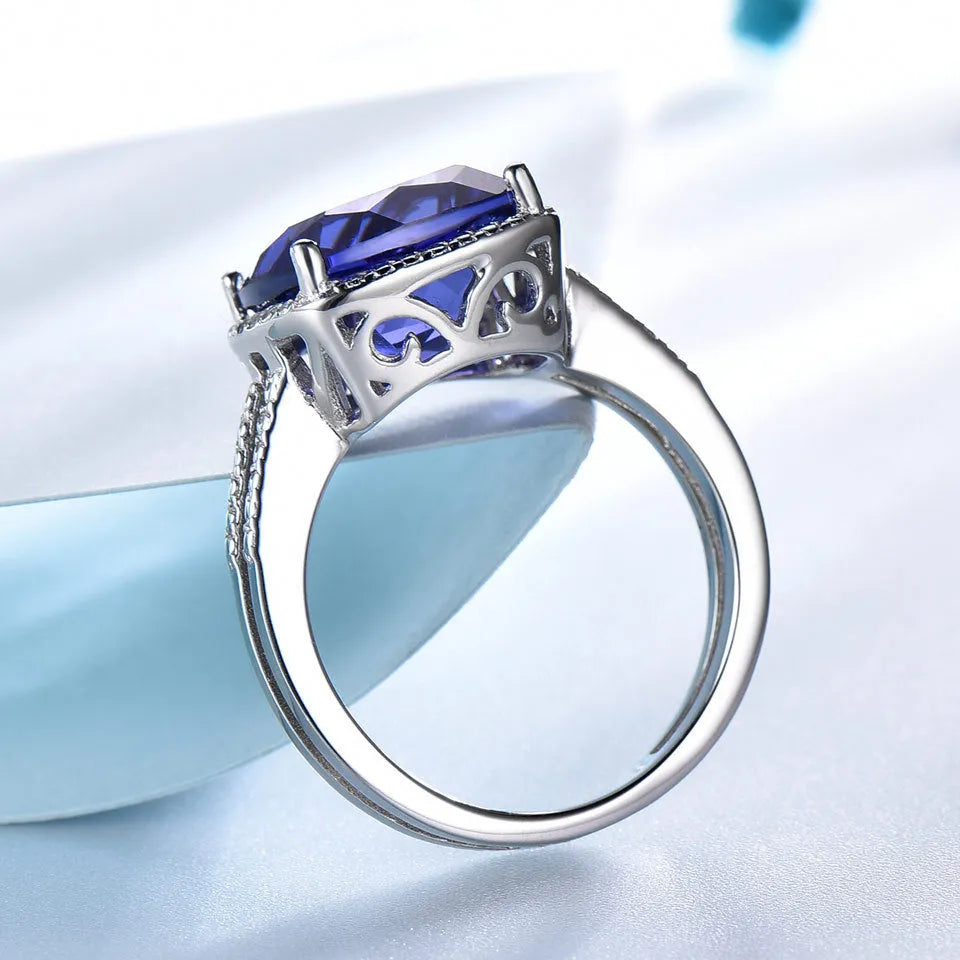Close-up of a blue tanzanite stone set in a sterling silver women's ring on a grey background.