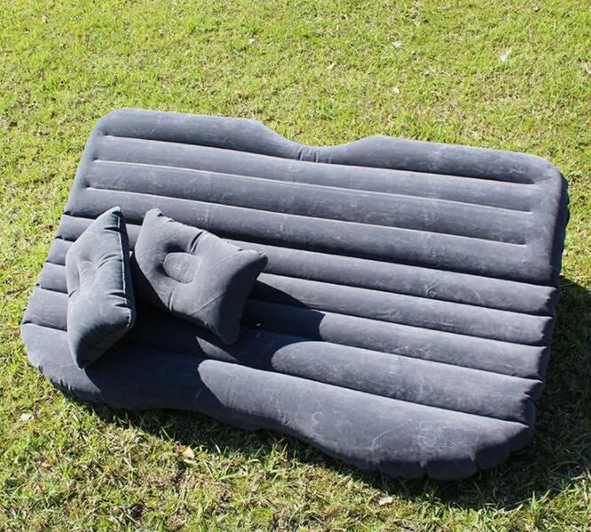 Black inflatable car bed with flocked surface and two pillows, shown inside a vehicle.