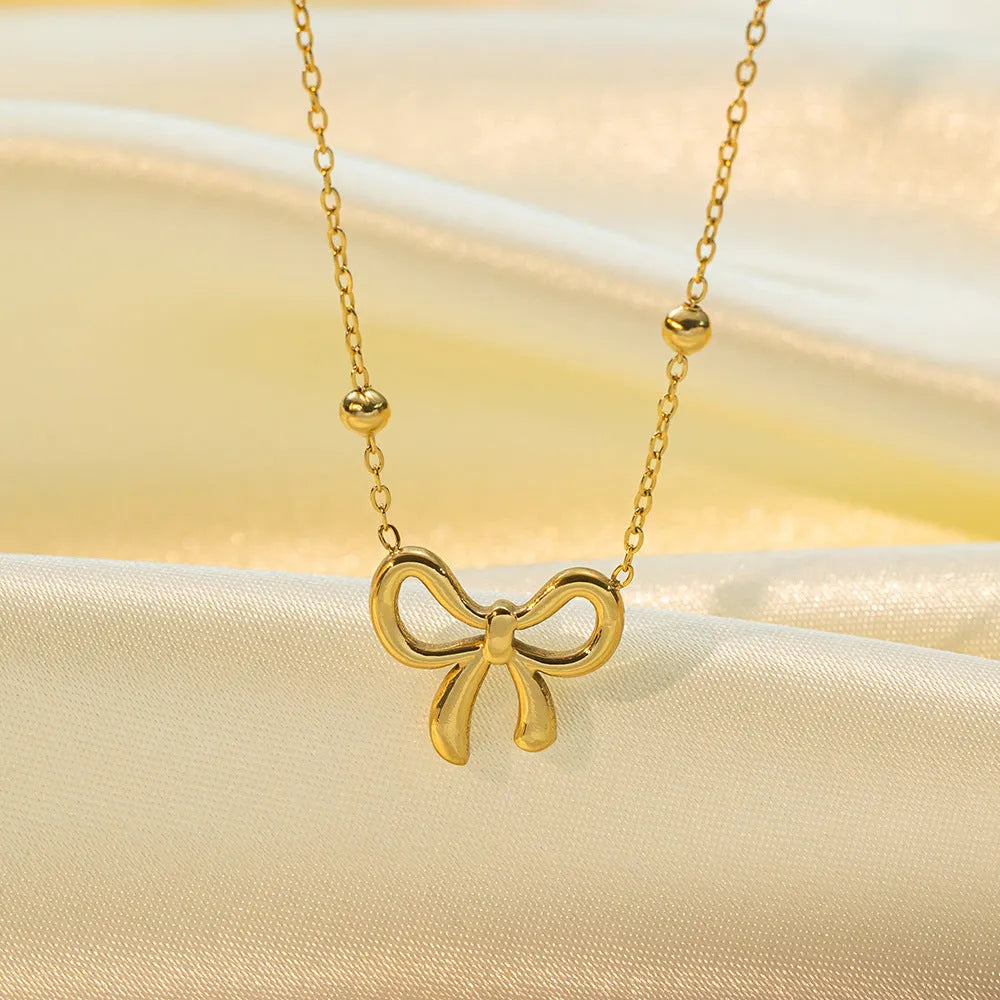 Gold electroplated bow necklace on a titanium steel cross chain, adjustable from 41 to 50 cm.