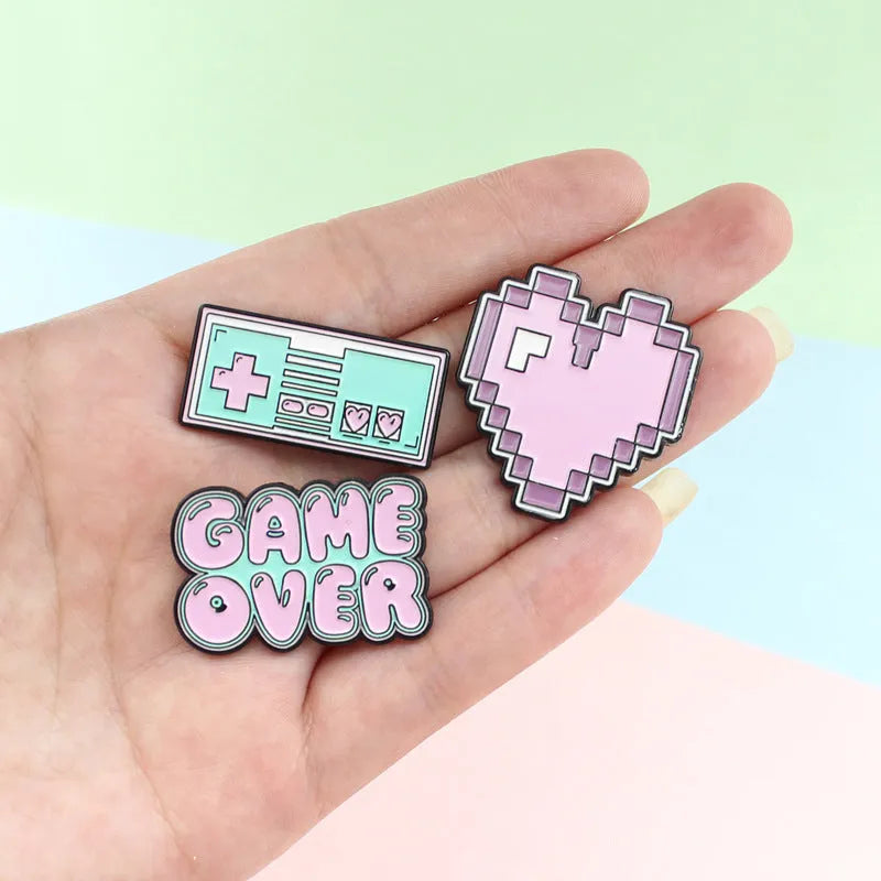 Stereo game console metal badge in protective OPP packaging, shown in one of three colour variants.