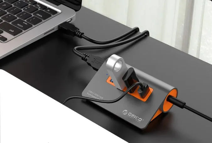 Dark grey and orange aluminium USB hub with four ports and a long black data cable.