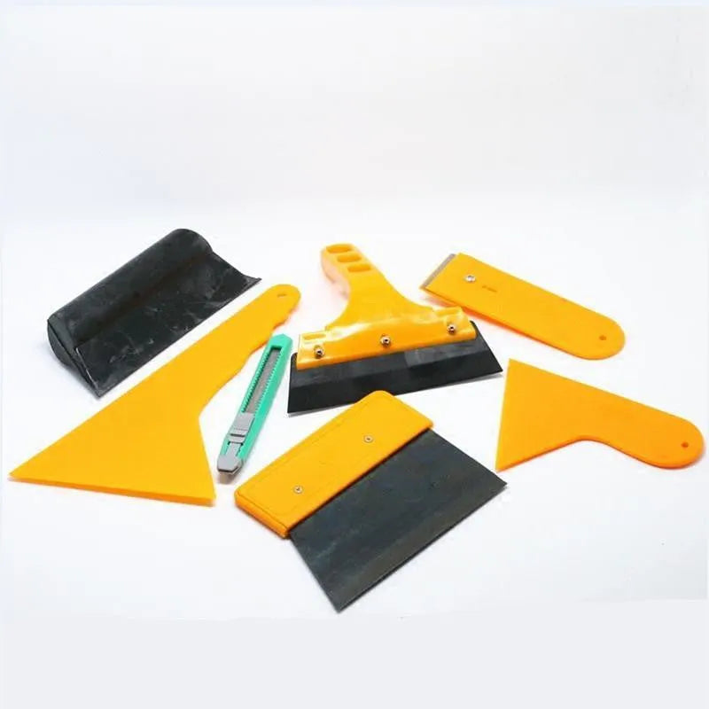 Seven-piece car film tool set with scrapers, knives, and a pressing block on a work surface.