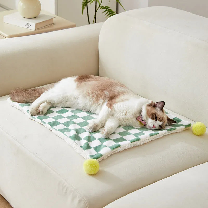 Green plaid pattern pet blanket with fur ball tassels on a sofa.