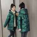 A woman wears a loose-fitting green hooded winter jacket with long sleeves.