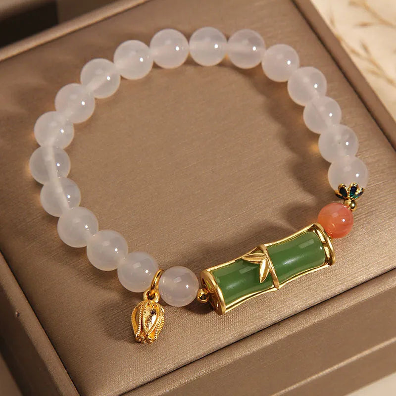 Women's bracelet with white agate bead and bamboo-shaped jade segments on a neutral background.