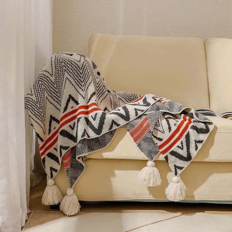 Beige and orange bohemian-style acrylic sofa blanket with tassel fringe on a grey sofa.