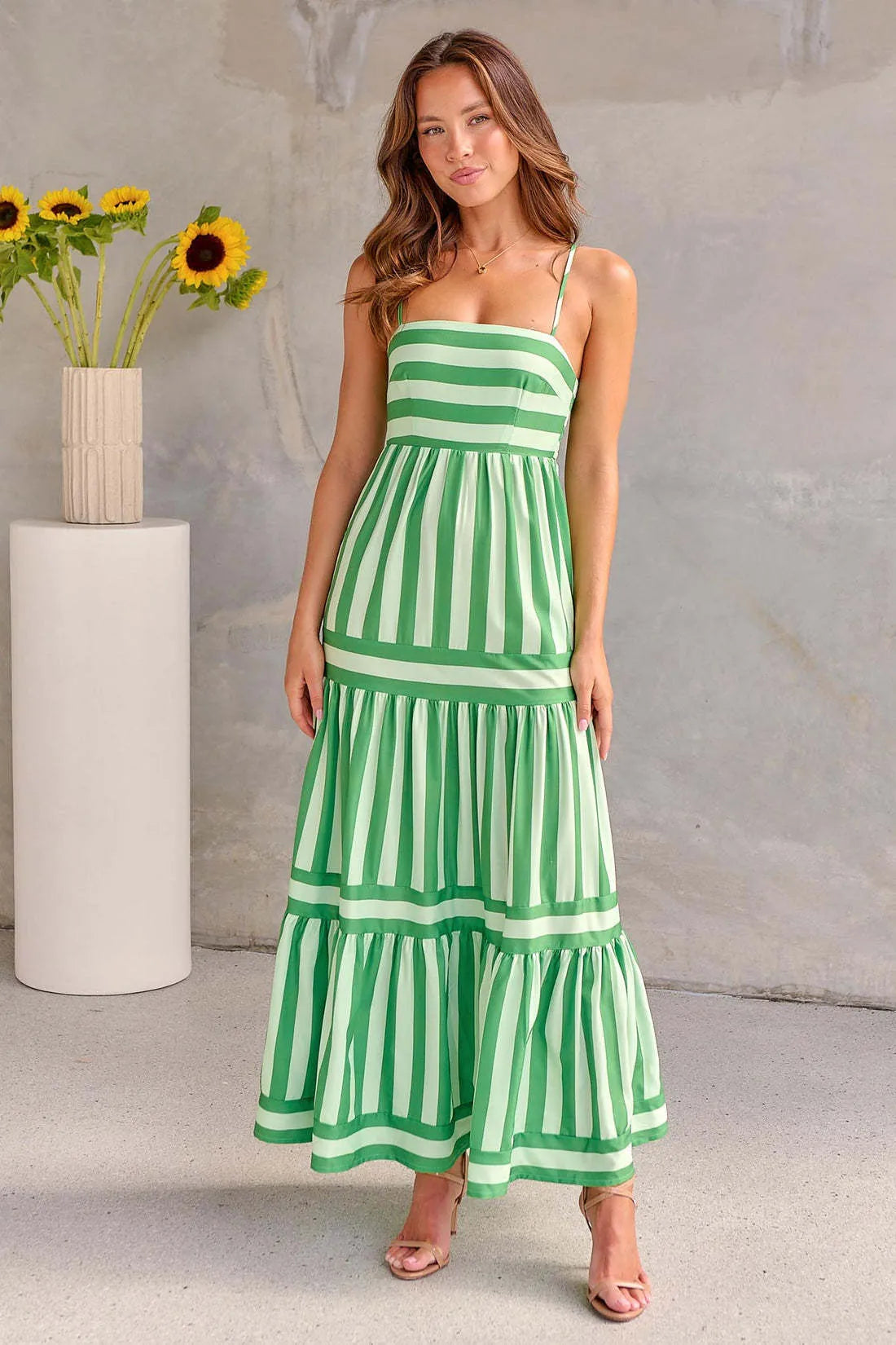 A woman wearing a striped backless suspender summer dress with a square neckline and side pockets.