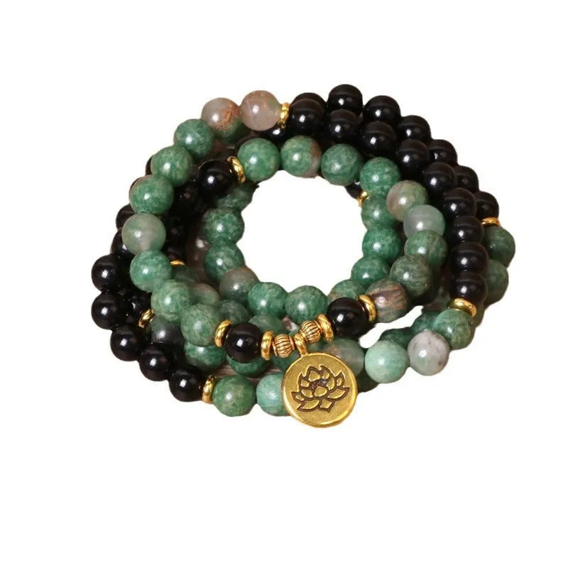 Green and black elastic beaded bracelet with metallic alloy charm details on a wrist.