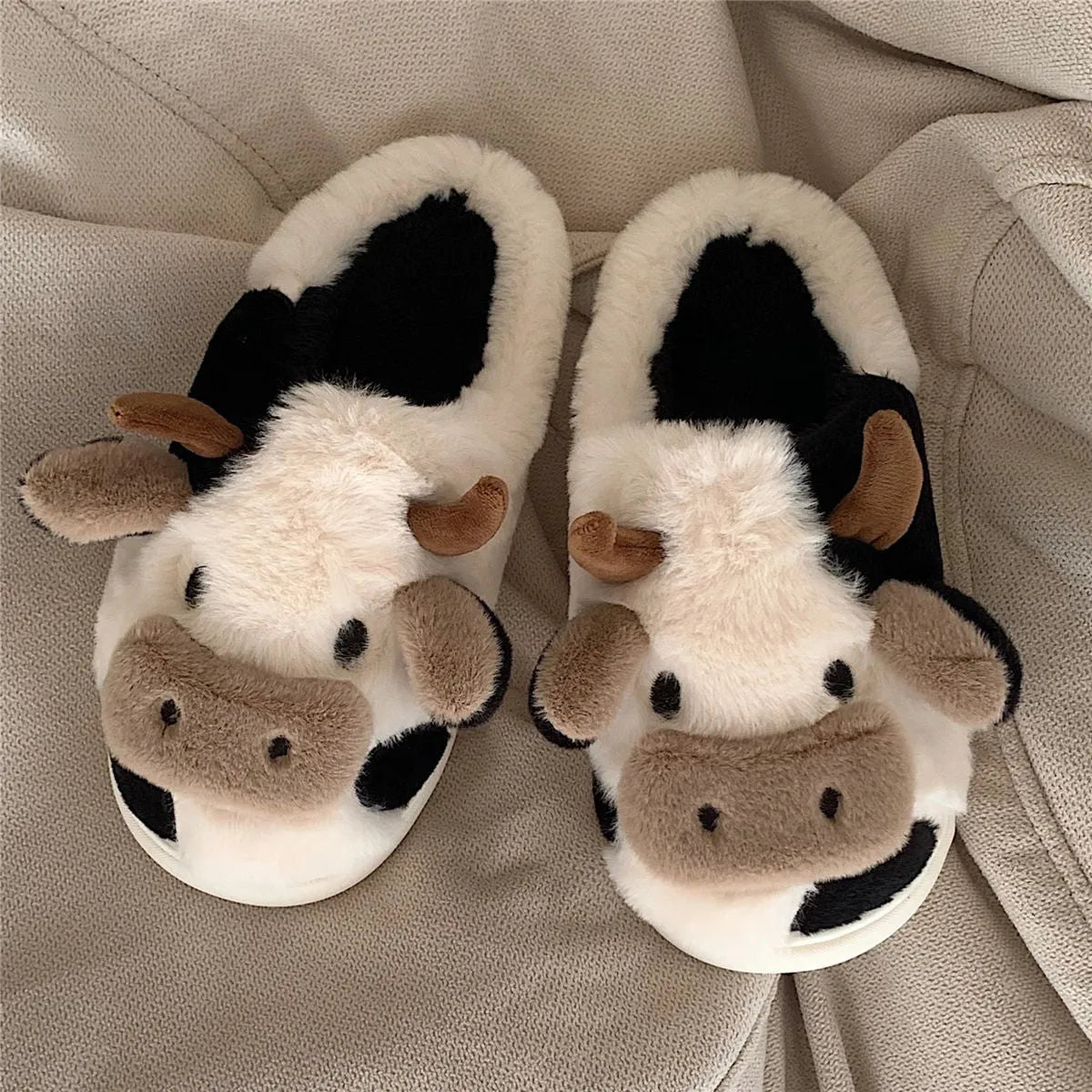 White cow plush slippers with non-slip textured soles shown from above
