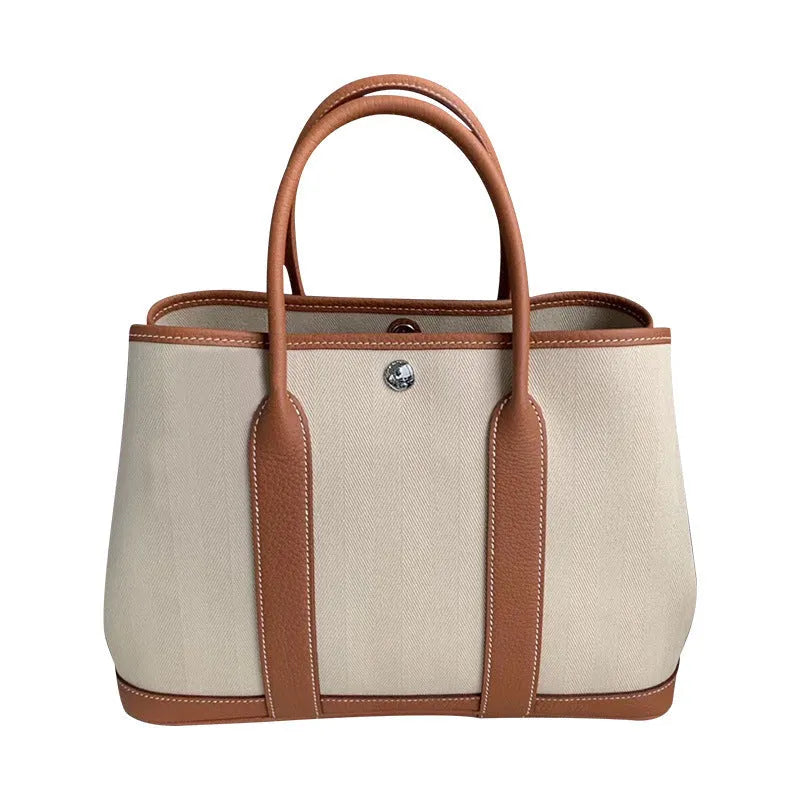 Women's canvas bucket tote bag with leather handles and detailing in black, shown with open top revealing internal zip pocket.