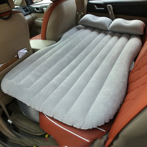 Black inflatable car bed with flocked surface and two pillows, shown inside a vehicle.