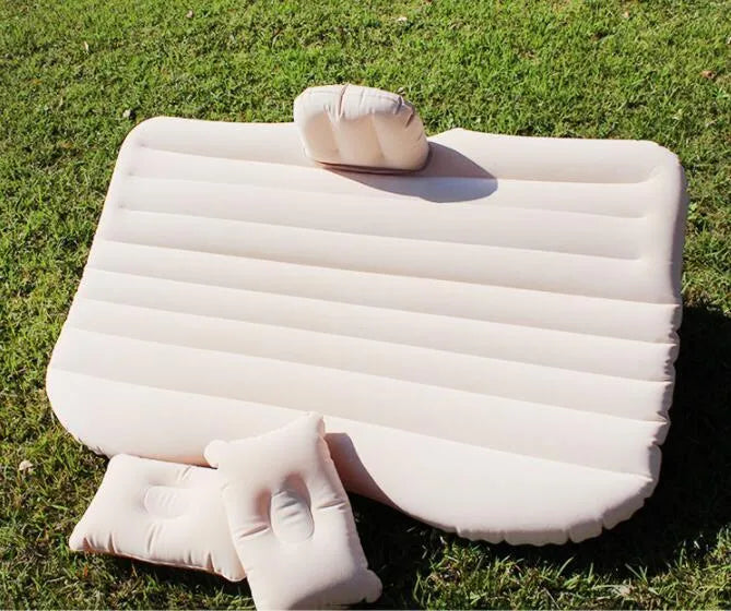 Black inflatable car bed with flocked surface and two pillows, shown inside a vehicle.
