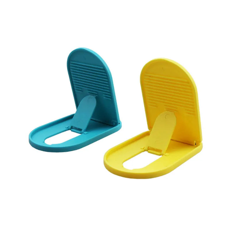 A lazy bracket style mobile phone stand made of plastic, shown in multiple colour options on a wooden desk.