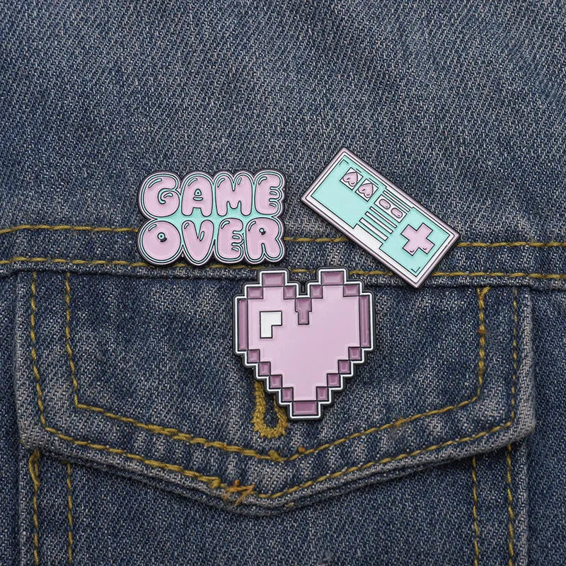 Stereo game console metal badge in protective OPP packaging, shown in one of three colour variants.