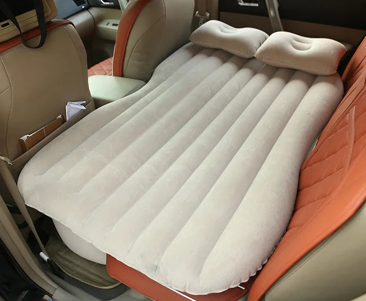Black inflatable car bed with flocked surface and two pillows, shown inside a vehicle.