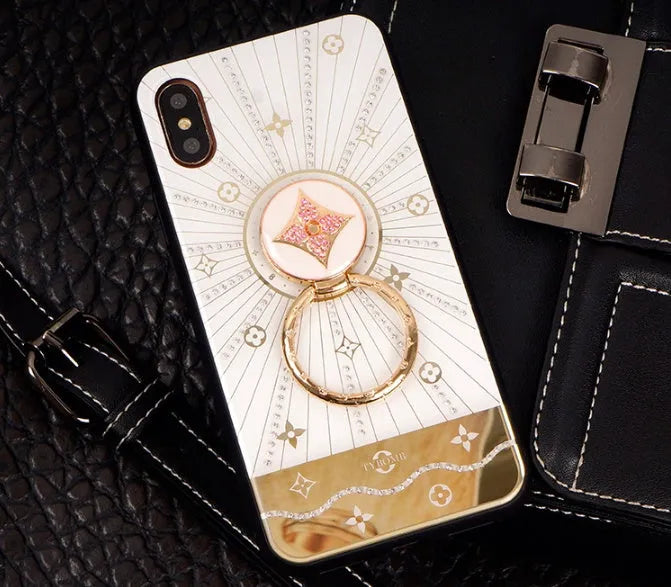 Gold-tone phone stand with diamond crystals holding iPhone and rings