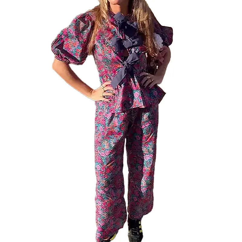 Women's floral print two-piece suit with a tie-neck puff sleeve top and matching trousers.