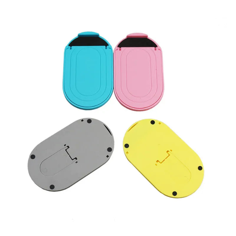 A lazy bracket style mobile phone stand made of plastic, shown in multiple colour options on a wooden desk.