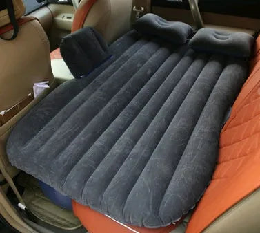 Black inflatable car bed with flocked surface and two pillows, shown inside a vehicle.