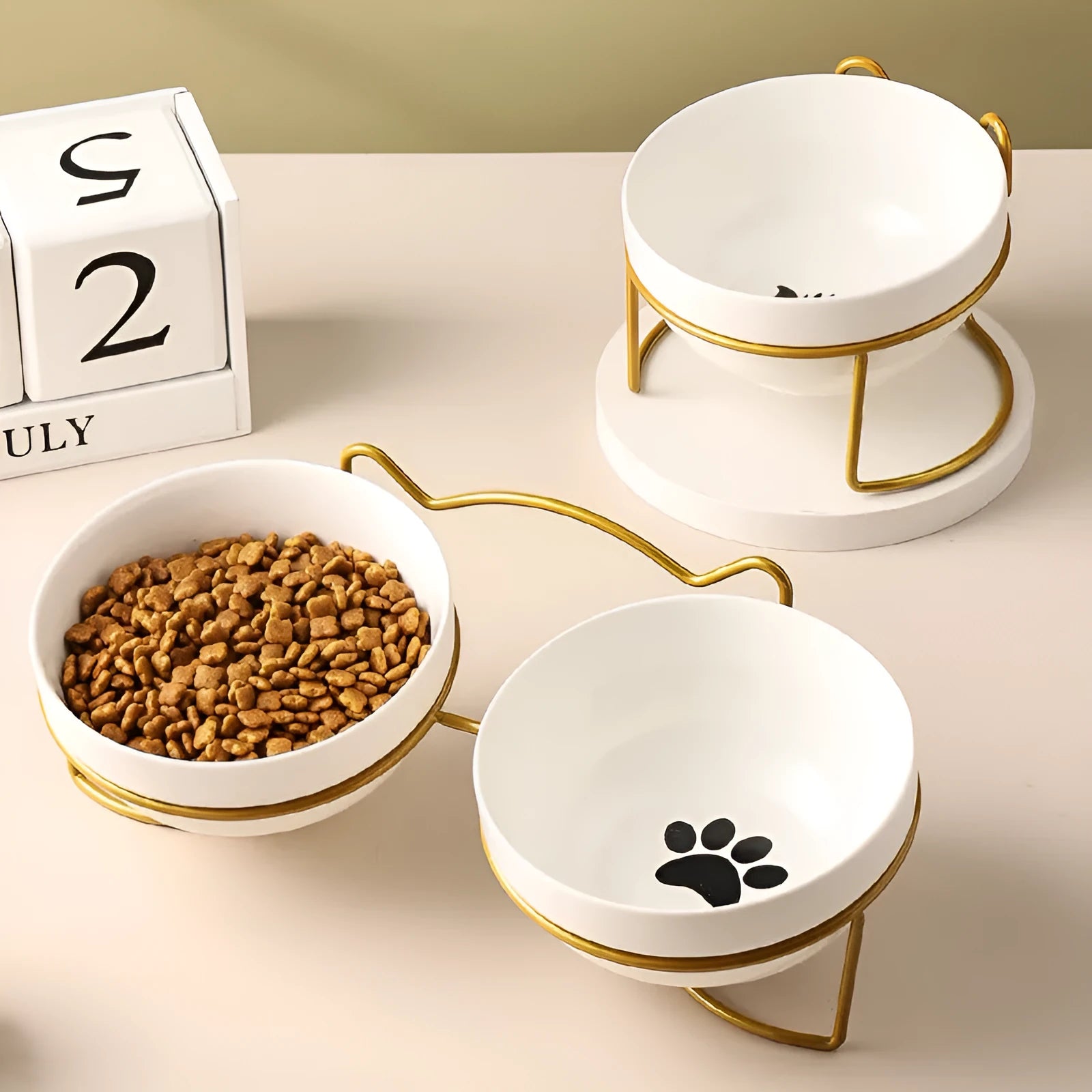 White ceramic pet bowl with cat paw print design on a black iron frame stand with cat ear details.