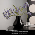 Ceramic round belly vase in black or white with artificial orchid stems on wooden surface