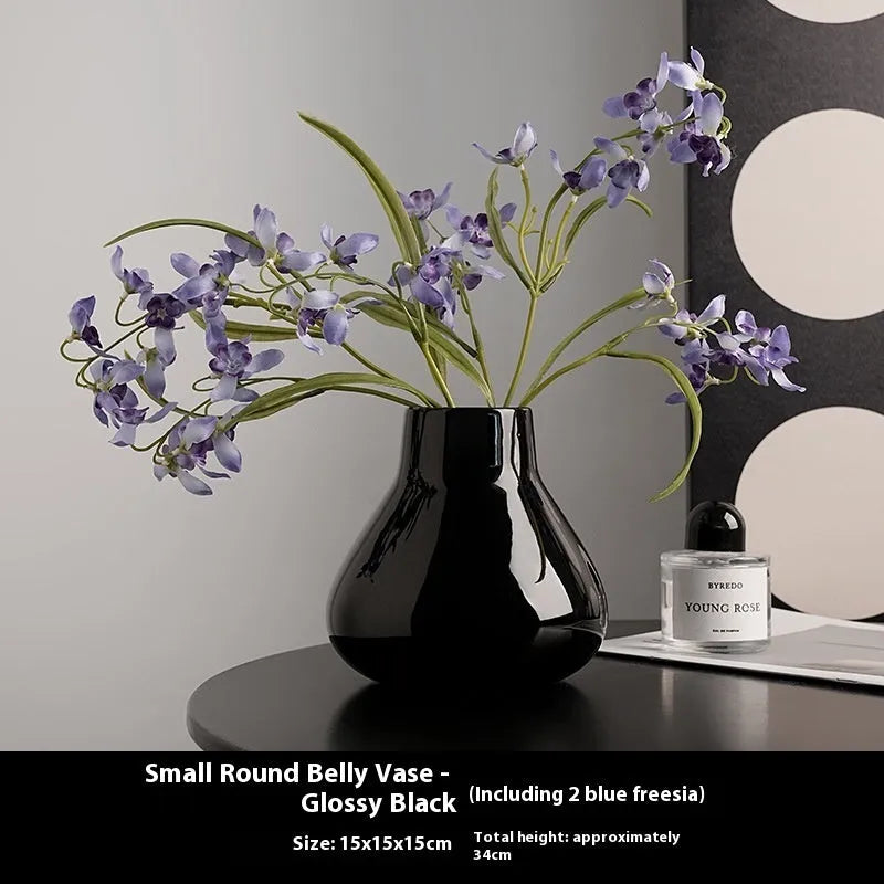 Ceramic round belly vase in black or white with artificial orchid stems on wooden surface